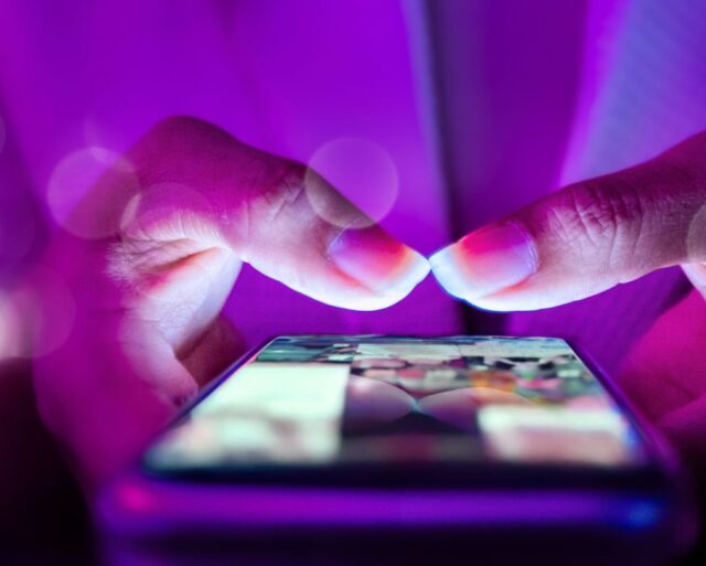 Hands holding a mobile phone surrounded by purple glow