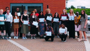 17 people including students holding exam results certificates and staff standing outside the Sutton Coldfield College A Level Centre