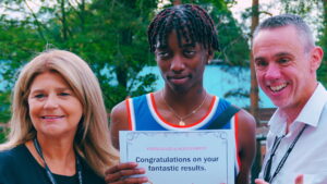 Student holding Certificate of Achievement featuring the the text: Congratulations on your fantastic results. A member of staff stands to the left and right of the student.