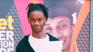 Male student holding a piece of paper with a poster advertising higher education courses in the background