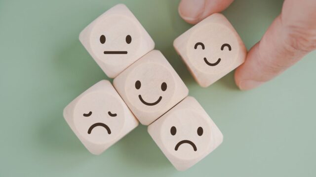 Five dice with simple face expressions, with one held by fingers