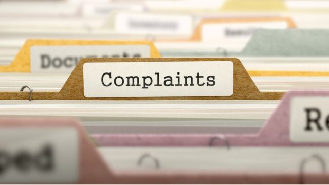 Papers files separated by tabbed dividers with sticker labelled 'Complaints' highlighted