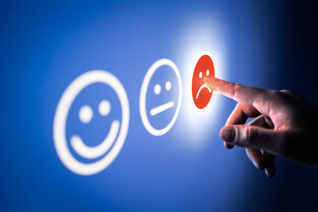 Blue screen with three simple face expressions and a hand pressing a red unhappy face