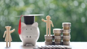 Wooden cut-out figures, piggy-bank and coins stacked together on white surface with green background