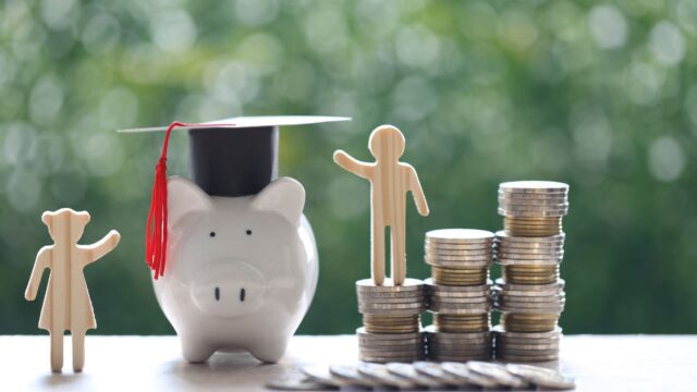 Wooden cut-out figures, piggy-bank and coins stacked together on white surface with green background