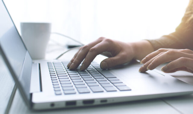 Close up of hand typing on a laptop and moving the mouse pad on a table with a white background
