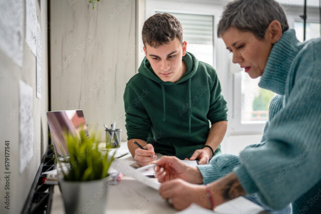 A male wearing a green top and female wearing blue top working with papers in a room with with pale walls